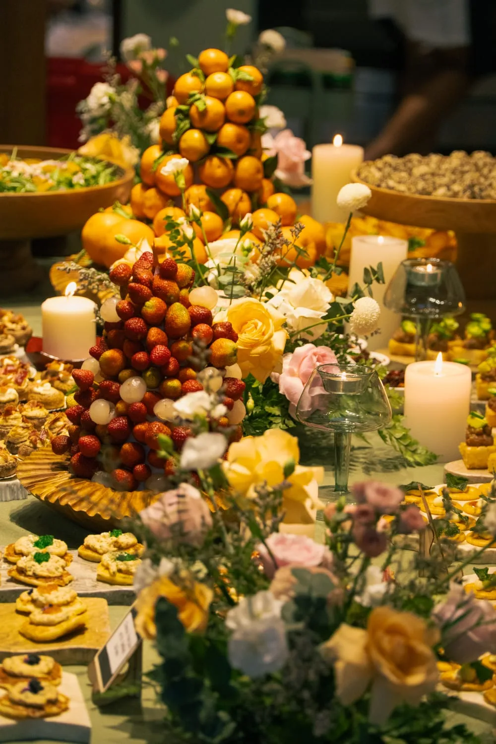 Grand grazing table with pyramids of strawberries and oranges, canapés and candlelight